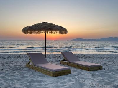 Dwa leżaki i słomkowy parawan na plaży o zachodzie słońca.