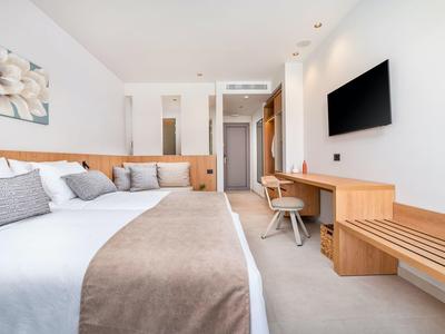 Nowoczesny pokój hotelowy z łóżkiem podwójnym, biurkiem, telewizorem i miejscem do siedzenia w neutralnych kolorach.