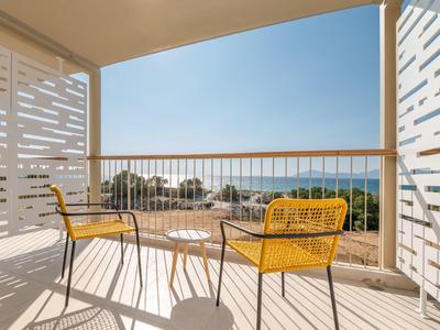 Balkon z dwoma żółtymi krzesłami i małym stolikiem z widokiem na morze w tle