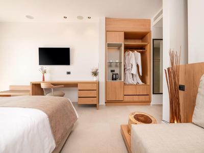 Nowoczesny pokój hotelowy z łóżkiem, telewizorem, biurkiem i otwartą szafą w neutralnych kolorach.