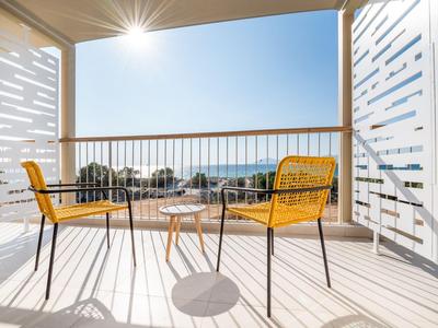 Balkon mit gelben Stühlen und kleinem Tisch mit Meerblick bei Sonnenschein.