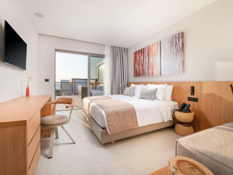 Nowoczesny pokój hotelowy z łóżkiem podwójnym, sztuką ścienną i balkonem z widokiem.