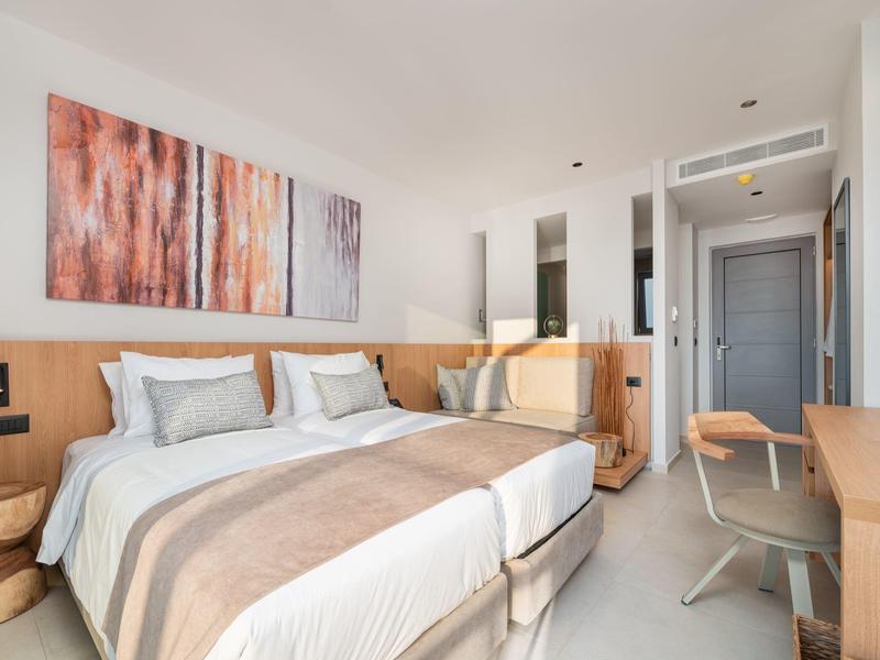 Nowoczesny pokój hotelowy z dwoma pojedynczymi łóżkami, drewnianymi meblami i jasnymi ścianami.