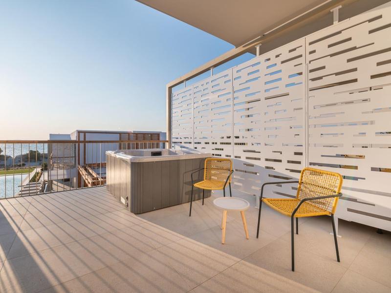 Nowoczesny balkon z dwoma krzesłami, małym stolikiem i jacuzzi z widokiem na morze.