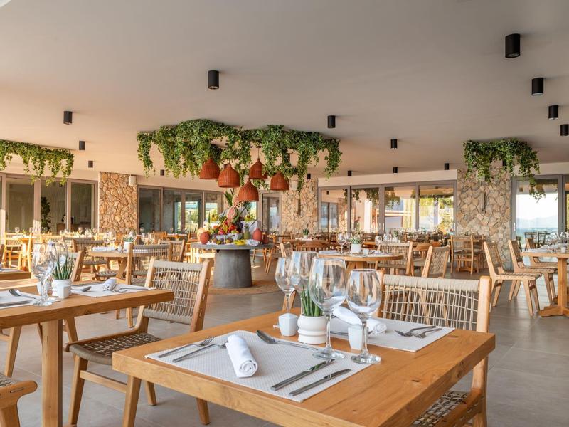 Jasna nowoczesna restauracja z drewnianymi stołami i wiszącymi roślinami jako dekoracja.