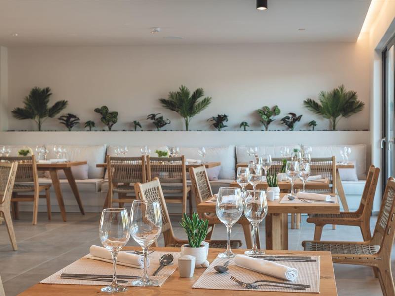 Nowoczesna restauracja z drewnianymi stolikami, białymi ścianami i roślinami jako dekoracją.