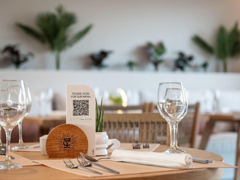 Elegancko nakryty stół w restauracji z kieliszkami do wina, sztućcami i roślinną dekoracją w tle.