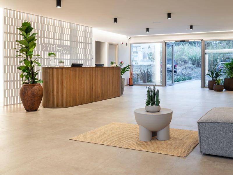 Jasne lobby hotelowe z drewnianą recepcją, dużymi roślinami i nowoczesnym miejscem do siedzenia.