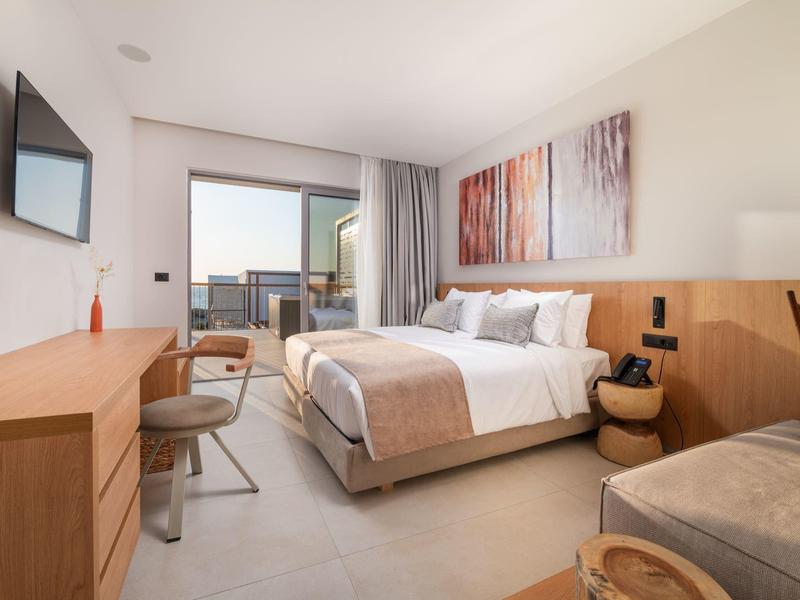 Nowoczesny pokój hotelowy z łóżkiem podwójnym, biurkiem, telewizorem i balkonem z widokiem.