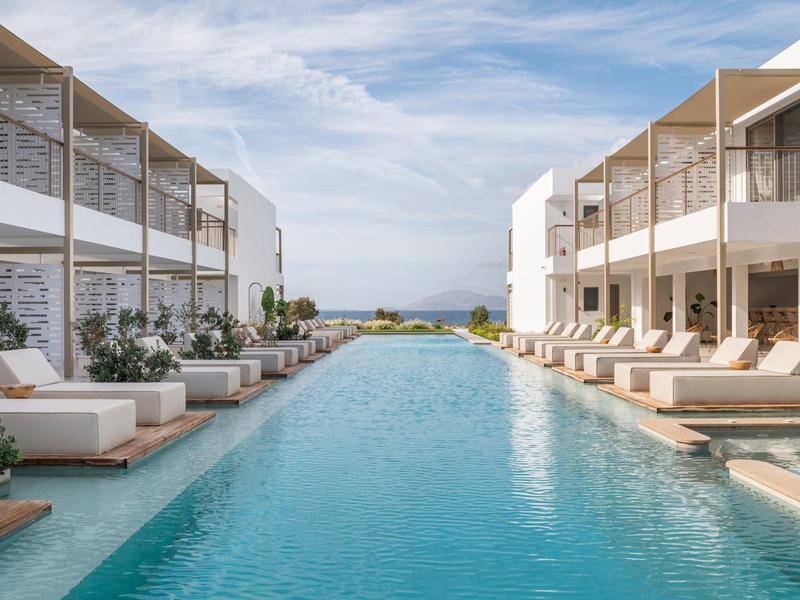 Nowoczesny basen na zewnątrz z leżakami między dwoma budynkami pod niebieskim niebem.