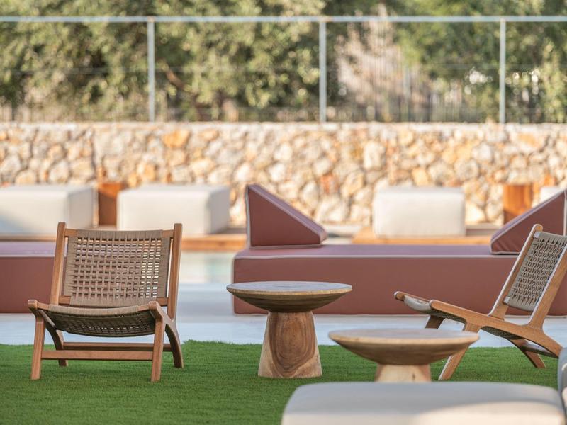 Wygodne drewniane meble z kanapami i stołami na zielonym trawniku przed kamiennym murem.