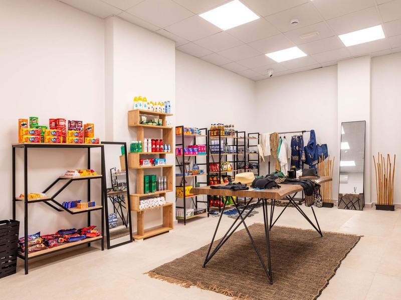 Jasno oświetlone pomieszczenie z półkami pełnymi kolorowych opakowań i stołem na środku na szarym dywanie.