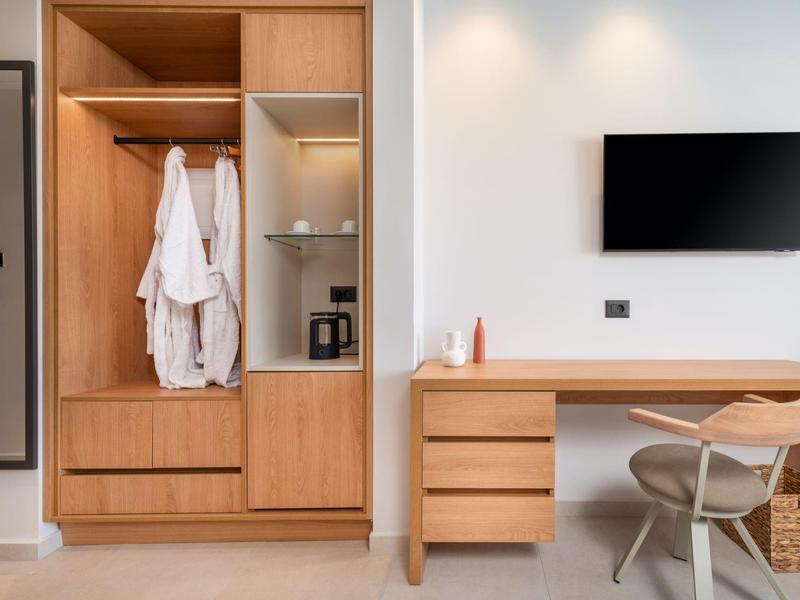 Nowoczesny pokój hotelowy z drewnianą szafą, biurkiem, krzesłem i telewizorem na ścianie.