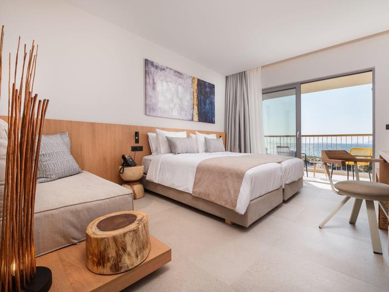 Jasny pokój hotelowy z podwójnym łóżkiem, miejscem do siedzenia i balkonem z widokiem na morze.