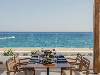 Esstisch mit vier Stühlen, gedeckt mit Wein und Essen, auf Terrasse mit Blick aufs blaue Meer.