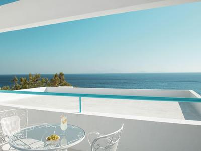 Weißer Balkon mit Glastisch, Stühlen und Meerblick unter klarem blauem Himmel.