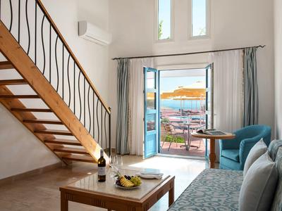 Světý obývací pokoj s dřevěnými trámy, pohovkou, stolem a výhledem na terasu s výhledem na moře.