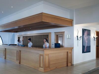 Große, helle Hotelrezeption mit Holzverkleidung und zwei Mitarbeitern hinter dem Tresen.