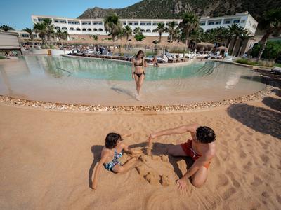 Kinder bauen am Sandstrand ein Sandhaus vor einem Pool in einem Hotelresort.