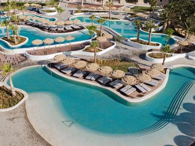 Große, geschwungene Poollandschaft mit Liegestühlen und Sonnenschirmen in tropischem Resort.