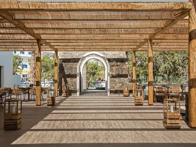 Krytá venkovní lounge s dřevěnými trámy, posezením a výhledem na kamenný oblouk.