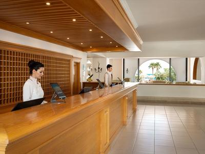 Přátelská hotelová recepce s dřevěným pultem a dvěma zaměstnanci na recepci.