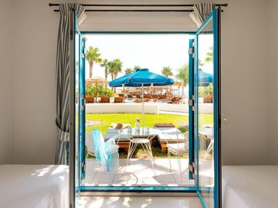 Blick durch offene Glastür auf Terrasse mit Stühlen, Rasen und Pool in tropischer Umgebung.