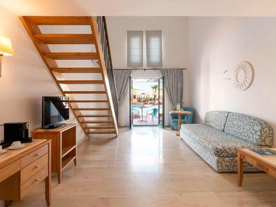 Heller Hotelzimmerbereich mit Treppe, Sofa, Schreibtisch und Blick auf Terrasse und Meer.