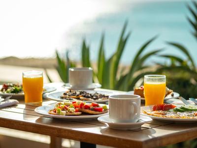 Frühstückstisch mit Saft, Kaffee und Speisen auf Holzterrasse mit Blick aufs Meer.