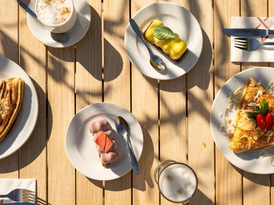 Verschiedene Frühstückspeisen und Getränke auf einem hölzernen Tisch bei Sonnenlicht.