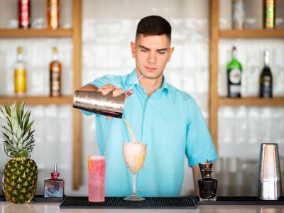 Mann in türkisfarbenem Hemd mixt Cocktail an einer Hotelbar mit Ananas und Spirituosen.