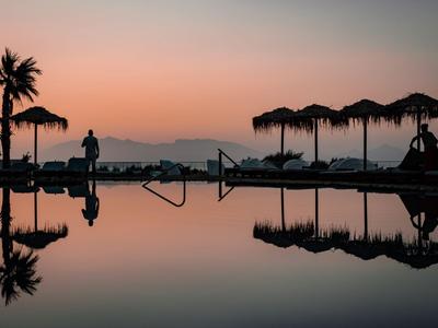 Ein ruhiger Pool bei Sonnenuntergang mit silhouettierten Menschen und Palmen am Hotelstrand.
