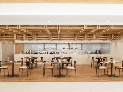 Moderner Hotelrestaurantbereich mit Holzdecke, Tischen und Stühlen in warmen Tönen.