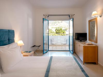 Helles Hotelzimmer mit komfortablem Bett und Balkon mit Blick auf einen Garten.