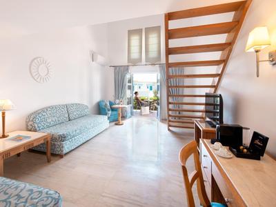 Helle Hotelzimmereinrichtung mit Treppe, Sofa, Schreibtisch und Blick auf einen weiteren Raum.