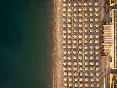 Vogelperspektive auf einen Strand mit Reihen von Sonnenschirmen und angrenzendem Hotelgebäude.