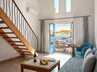 Helles Wohnzimmer mit Holztreppe und offenem Türzugang zu Terrasse und Meerblick.