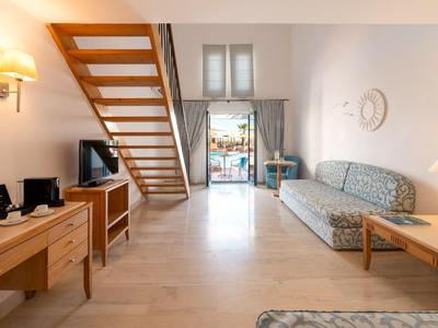 Heller Wohnzimmerbereich mit Holztreppe, Sofa und Zugang zu Balkon in einem Hotelzimmer.