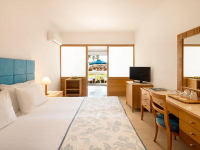 Modernes Hotelzimmer mit großem Bett, Schreibtisch und Blick auf Terrasse mit Pool.