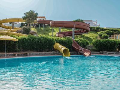 Wasserrutschen führen in einen großen Pool mit klarem Wasser, umgeben von grüner Landschaft.