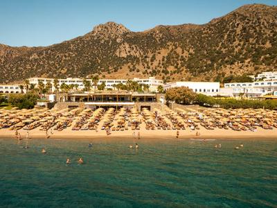 Ein Hotel mit Pool und vielen Strandliegen vor einer Bergkulisse am blauen Meer.