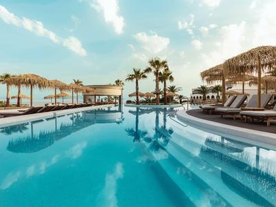 Ein großer Pool mit Liegestühlen und Palmen unter einem bewölkten Himmel in einem Hotelresort.