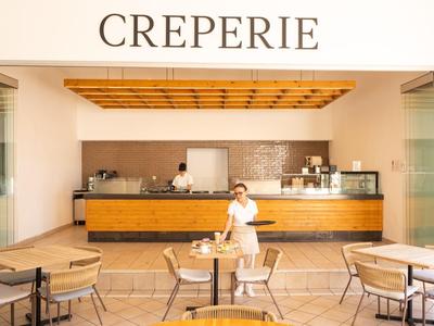 Offene Crêperie mit Holzdecke, Tischen und Stühlen, Bedienung in weißem Hemd.