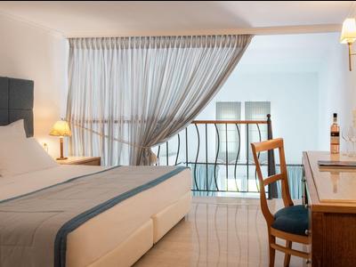 Helles Hotelzimmer mit Doppelbett, Schreibtisch und Balkon mit Blick auf Innenraum.