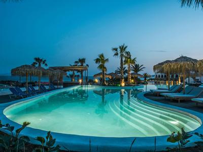Beleuchteter Swimmingpool mit Liegestühlen und Palmen bei Dämmerung in einem Resort.