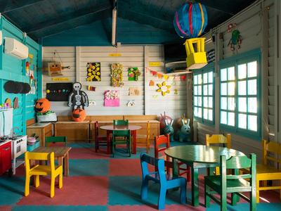 Bunt eingerichteter Kinderbereich mit Spielzeug, bunten Stühlen und Fenster mit Vorhängen.