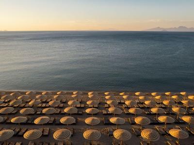 Geordnete Sonnenschirme am Strand vor ruhigem Meer bei Sonnenuntergang.