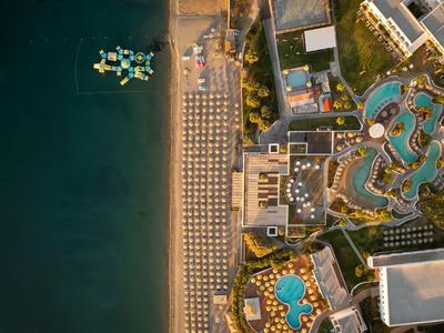 Vogelperspektive eines Resorts mit Pool, Strandliegen und Meer mit Booten.