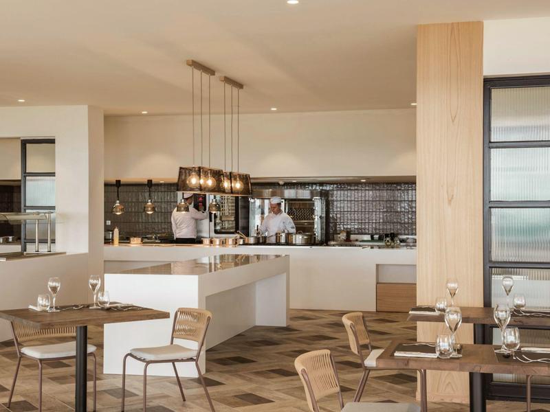 Moderní jídelní prostor restaurace se dřevěnými stoly, židlemi a kuchyní na pozadí.