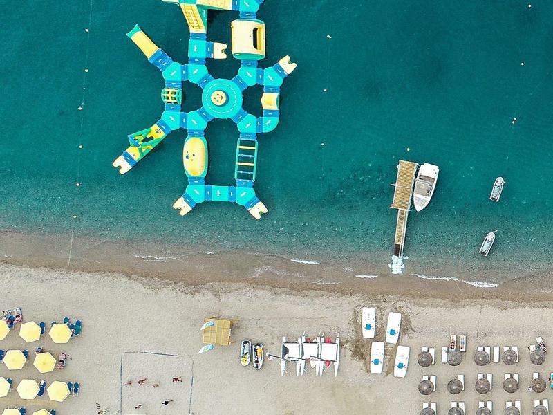 Letecký pohled na pláž s řadami slunečníků, lehátek a velkým nafukovacím vodním parkem.